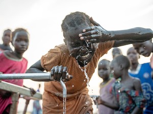 © UNICEF/UN0836989/Naftalin / Ein Mädchen im Südsudan kühlt ihren Kopf an einer Wasserstelle. Im Südsudan und vielen anderen Ländern hat die Zahl der extrem heißen Tage stark zugenommen